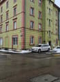 Corner building with four floors, light green color with red frames around the windows, snow on the ground, a parked car in front, two other buildings next to it