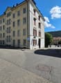 4 story building, yellow exterior, red window shutters, blue handicap parking sign, corner street, cars parked on the street