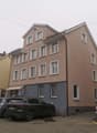 Three-story house with multiple windows, beige facade, awning, parking area
