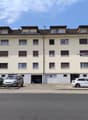 4 story apartment building, beige exterior, multiple windows, garage, multiple cars parked in front