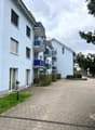 Blue apartment building with multiple balconies, brick paved driveway, hedges, trees