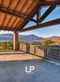 Covered outdoor terrace with wooden beams and tiled flooring, offering a scenic view of the surrounding mountains and lake in the distance.