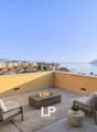 Balcony with chairs, fire pit, potted plants, lamps, rug, view of the city and sea