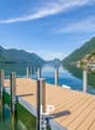 Scenic view of a lake surrounded by mountains, with a wooden dock in the foreground and buildings on the shore in the distance.