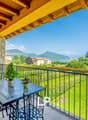 Balcony with a table and chairs, overlooking a lush green garden and scenic mountain landscape. The balcony has a wooden ceiling with exposed beams.