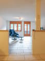 Spacious living room with large windows, wooden furniture, and a balcony or terrace visible through the glass doors.
