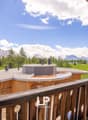 Balcony overlooking a scenic mountain landscape with snow-capped peaks, green meadows, and a fountain or water feature in the foreground. The balcony has a wooden railing and the apartment building appears to be in a resort or alpine setting.