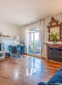 Spacious living room with hardwood floors, large windows, ornate gold-framed mirror, fireplace, TV entertainment unit, and dining area with glass table and chairs