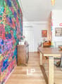 Colorful graffiti-style mural wall, wooden dining table with chairs, shelving unit, and a fireplace visible in the room.