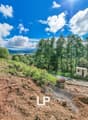 Excavations site, sloped land, grassy areas, trees, distant mountain views, lake in the distance, pathway, utility pole