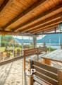 Enclosed terrace, wooden benches and table, glass walls, hanging lamp, view of mountains and water, decorative potted plants on ground
