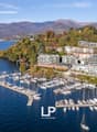 Marina with many boats docked, surrounded by mountains and a lake, multiple residential buildings