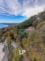 House on hillside, view of lake and city, trees, dirt road, another house in background