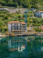 Terraced houses with various architectural designs and colors, under construction buildings, a crane, surrounded by trees and mountains, reflecting on the calm lake