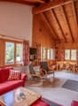 wooden walls and ceiling, fireplace, large windows with mountain views, red sofa, wooden coffee table, dining table and chairs