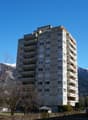 High-rise building with multiple floors and balconies, surrounded by trees and mountains