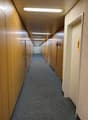 long hallway with wooden lockers on both sides, gray carpet flooring, white ceilings with LED lighting, door at the end