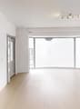 Spacious living room with large windows, hardwood floors, and track lighting. The room has a balcony or terrace visible through the windows.