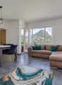 Spacious open-plan living area with large windows offering a scenic mountain view, a comfortable brown sofa, a dining table with black chairs, and a modern light fixture overhead.