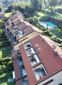 Multi-story apartment buildings with red tile roofs, surrounded by lush greenery and a swimming pool in the center of the complex