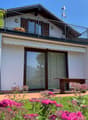 2-story house with a balcony, white exterior walls, large windows, and a landscaped garden with pink flowers in the foreground.