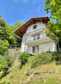 modern design two-story house, white exterior, wooden balcony, lush greenery around