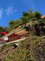 Red and white house, large balcony, red roof, balcony railing, surrounded by greenery and trees