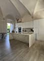 white modern kitchen with marble countertop, central island with sink, dining table with chairs, window with view to garden