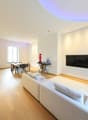 large living room with sofa, coffee table, dining area with table and chairs, flat screen TV, large window, wood flooring