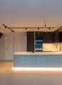 Modern kitchen with open floor plan, sleek black metal staircase, white countertops, integrated sink, and recessed lighting.