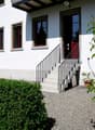 white house, red door, concrete steps, gravel driveway, hedges, trees
