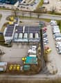 Aerial view of a parking lot with multiple vehicles parked, a building with solar panels, and a road with cars.