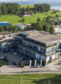 4 story building, surrounded by parking lot, several parked cars, landscaped gardens, hilly green surroundings