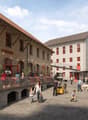 Two buildings with red windows and doors, people sitting at tables on a balcony, a truck, a small garden, and a bicycle on the ground.