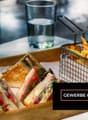 A wooden tray with sandwiches and french fries, two glasses of water, and a basket of fries