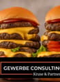 Two hamburgers stacked on top of each other, with multiple layers of beef patties, cheese, lettuce, and tomato.