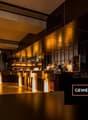 modern bar with wooden counters, yellow lighting, shelves with bottles, chalkboard menu, plant