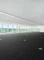 Large open office space with floor-to-ceiling windows offering a panoramic view of the surrounding landscape. The room has a black carpeted floor and recessed lighting in the ceiling.
