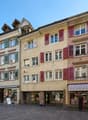 2-story building, red shutters, large windows, ground floor storefronts, cobblestone street