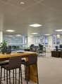 Large open-plan office space with modern furniture and amenities. The space features a kitchen area with a dishwasher, as well as multiple workstations and a communal dining/meeting table.