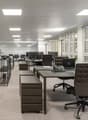 Modern office space with contemporary furnishings, white walls, large windows, beige carpeting, and various office equipment