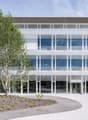 modern building, large glass windows, multiple floors, concrete facade with white vertical slats, main entrance, tree in front
