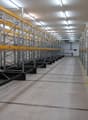 Rows of pallet racking system, numbered shelves, yellow and silver construction, fluorescent ceiling lights, clean and spacious with yellow lines on the floor