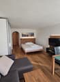 A room with a bed, couch, TV, dining table, and chairs.