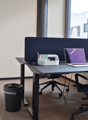 Office desk, office chair, laptop, trash bin, coat rack, large window with view outside