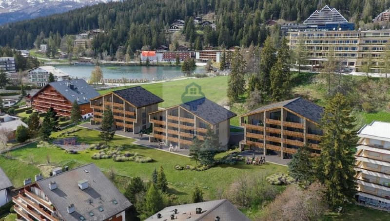Wooden apartment complex, mountain backdrop, near a lake, greenery