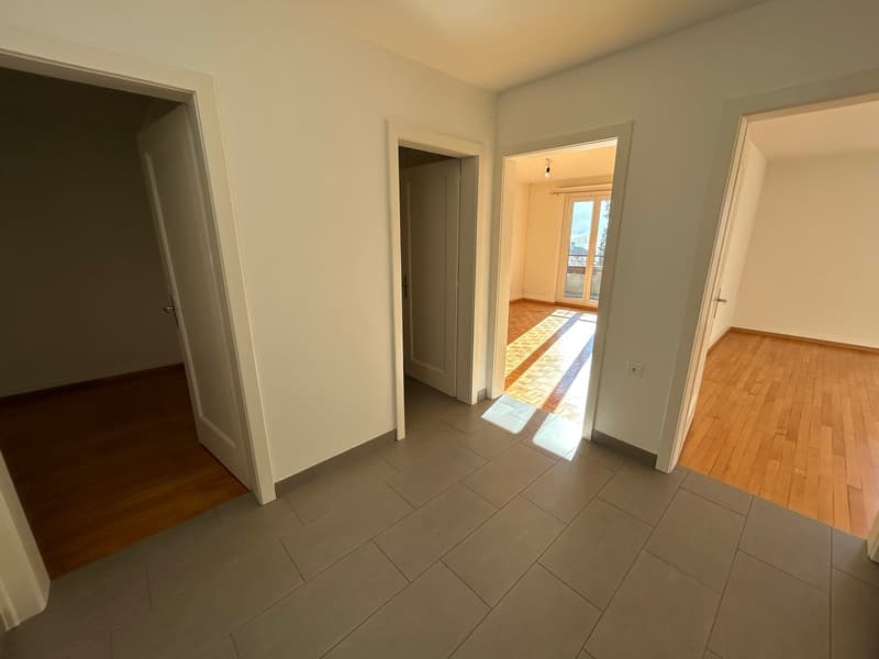 Empty room with gray tiles and wooden floors, sliding door leading to balcony with railings