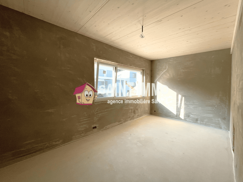 Unfinished room with bare walls and ceiling, large window, and an agency logo on the wall.