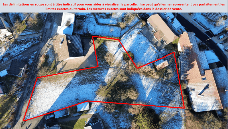 Several buildings are visible, with one large building covered in snow. There are trees, plants, and a paved driveway around the perimeter.
