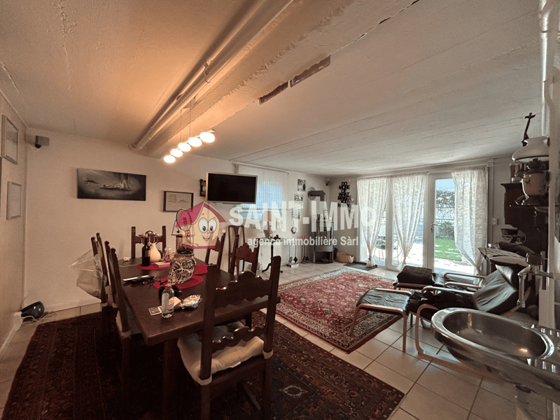 Spacious living room with hardwood floors, large windows, dining table, and various decorative items. The room has a cozy and homely feel.